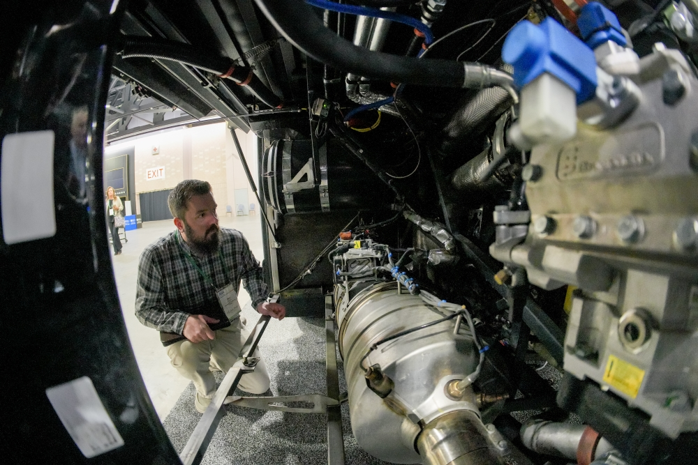 An image taken from within the interior of a bus where its wiring and mechanical elements are visible. A repair technician is inspecting the vehicle, adhering to property safety and maintenance for safe motorcoach operations.