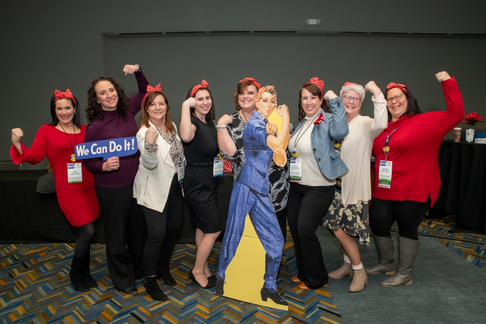 An image showing ABA Women in Buses council members standing with a Rosie the Riveter cut-out. The women are all mirroring Rosie's strong arm pose.