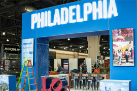 An image of a bus industry event, showing a large blue archway being constructed at the event space. The archway has large white letters spelling Philadelphia.